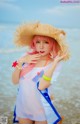 A woman with pink hair wearing a straw hat on the beach.