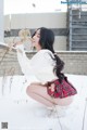 A woman in a white sweater and plaid skirt crouching in the snow.