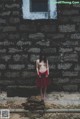 A woman in a red dress standing in front of a stone wall.