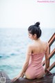 A woman in a pink bathing suit sitting on a wooden dock.