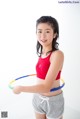 A young woman in a red top and gray shorts holding a hula hoop.